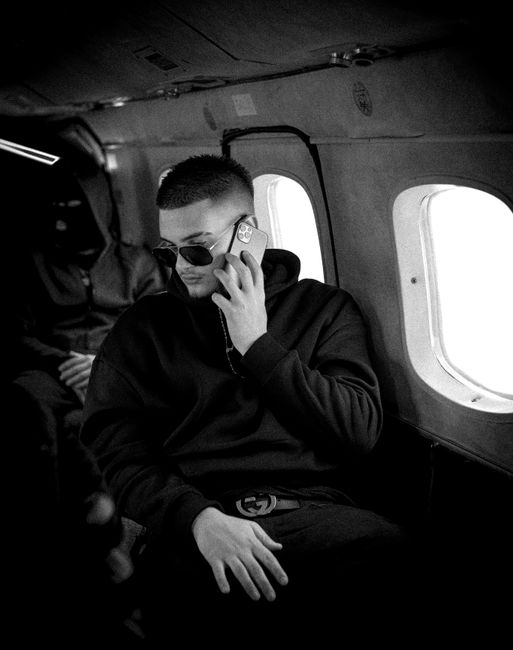 Photo by DYLBER CAUSHI Black and white image of a man using a smartphone inside an airplane cabin for communication.