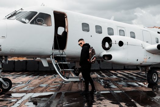 A man with a backpack boards a private jet on a wet airport tarmac in Tirana, Albania.