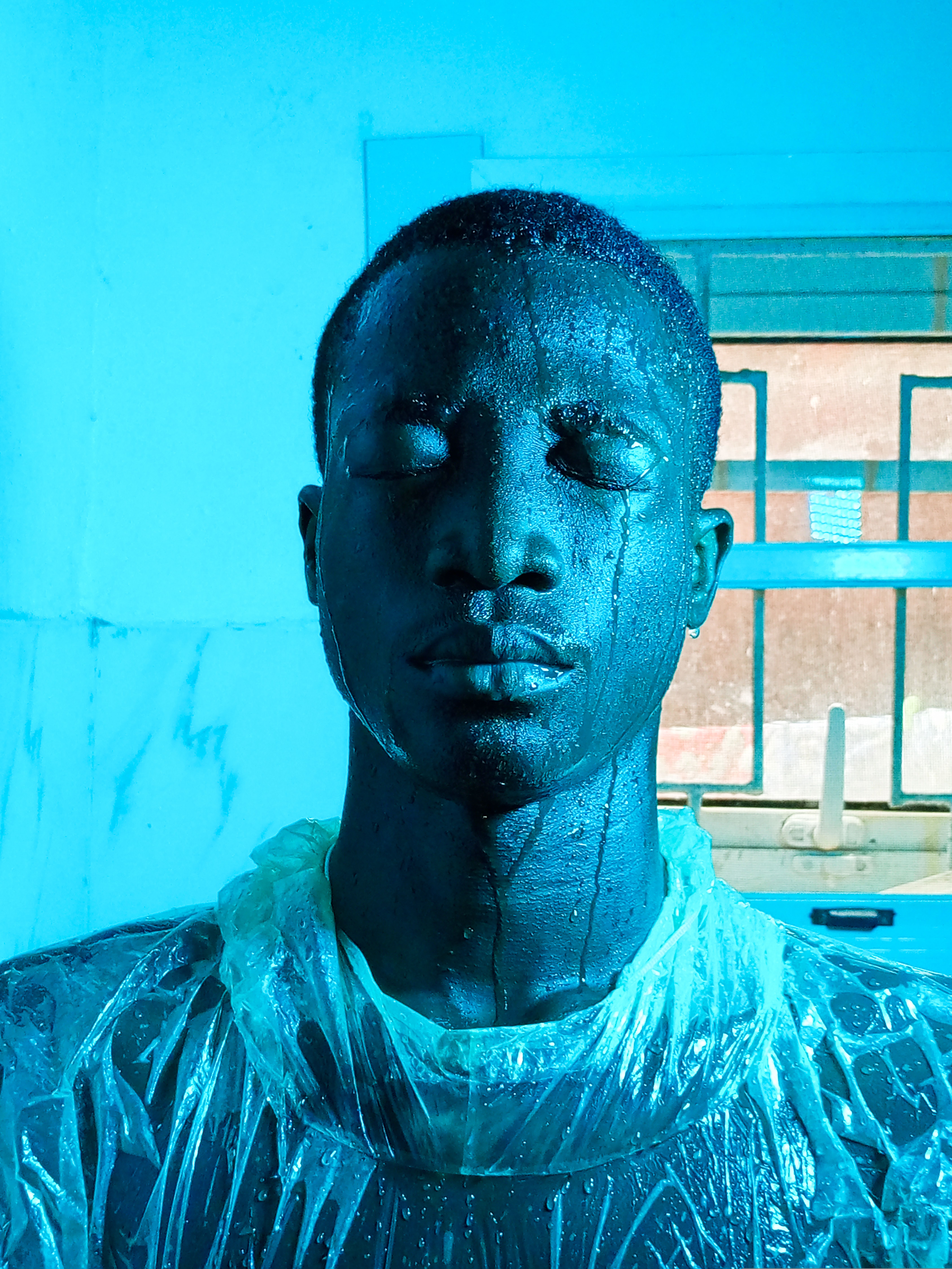 Striking portrait of a man in a foil suit, drenched, eyes closed under blue lighting.