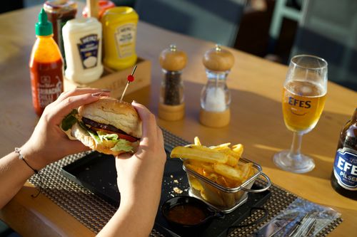 Free A person enjoying a delicious burger and fries with a glass of beer at a restaurant. Stock Photo