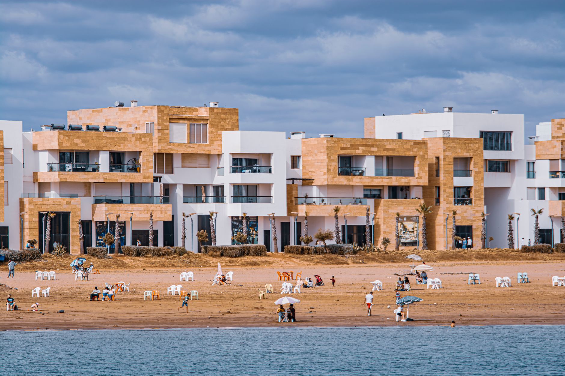Coastal view of modern apartments and people enjoying a peaceful day at the beach.