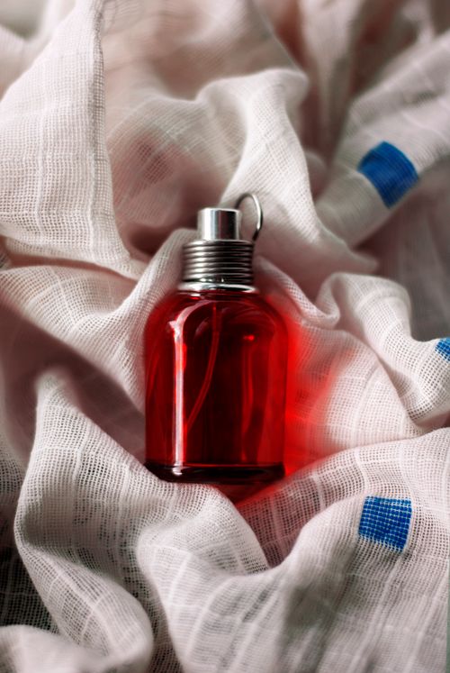 Free A striking red perfume bottle elegantly displayed on a textured fabric with blue accents, creating a sophisticated still life composition. Stock Photo
