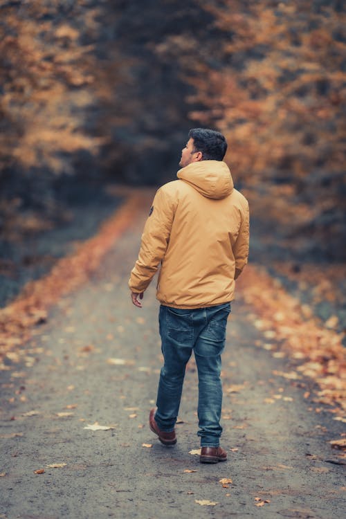 Man in a Yellow Jacket and Jeans on the Road Through the Autumn Forest