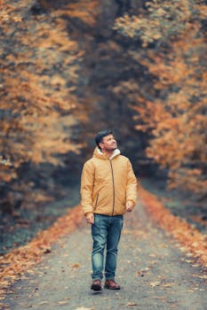 A man in a jacket walks through a vibrant autumn forest, enjoying the fall colors.