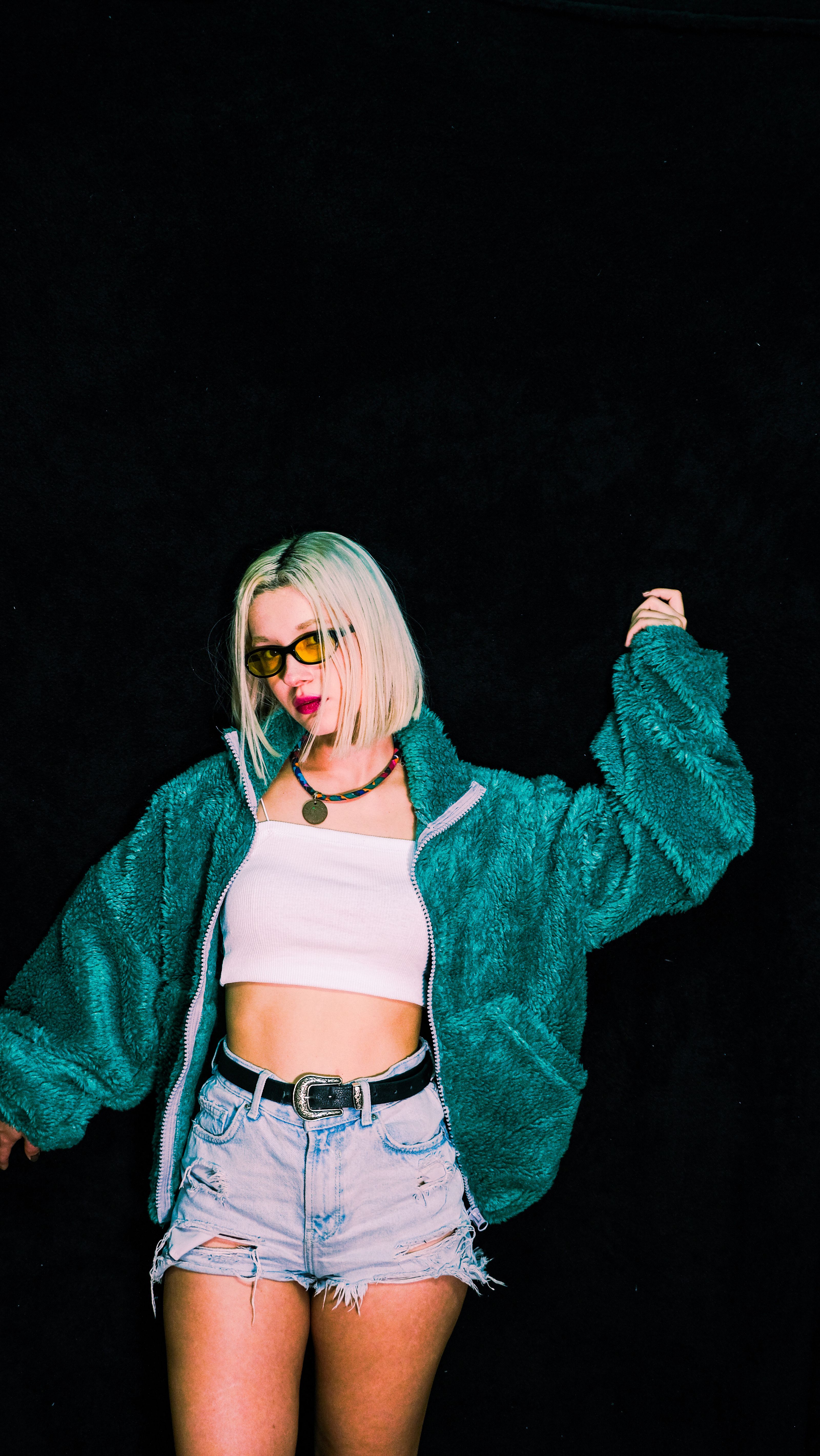 Jovem mulher posa com confiança em shorts jeans e jaqueta verde, exibindo moda moderna.