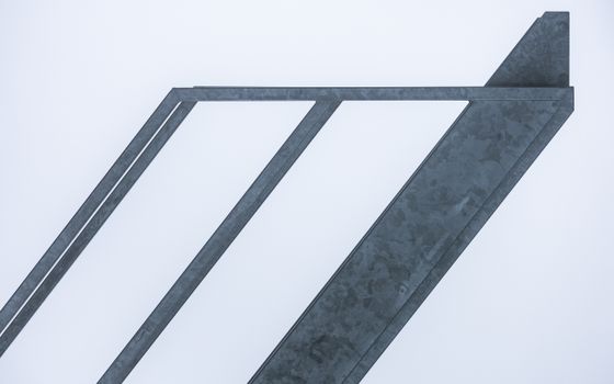 Minimalist view of abstract diagonal metal beams set against a clear sky.