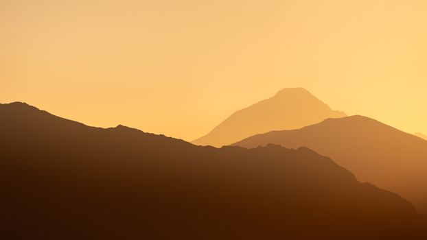 Captivating mountain silhouette with warm hues of sunrise casting a dramatic glow.