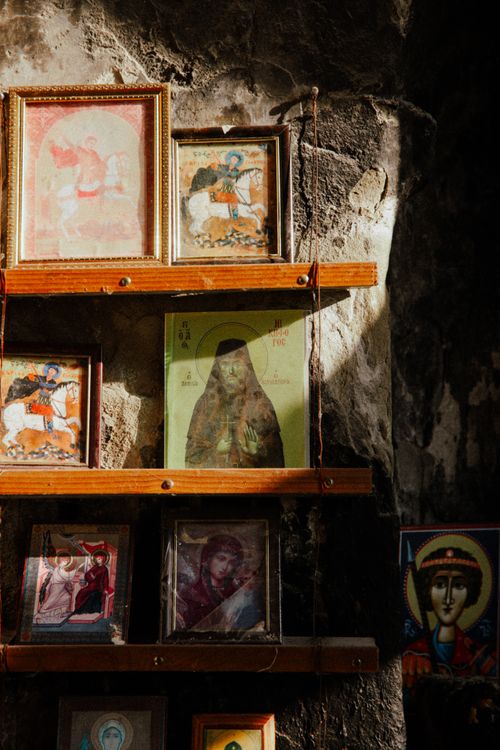 Free A collection of framed religious icons on shelves, illuminated by natural light inside an old church. Stock Photo