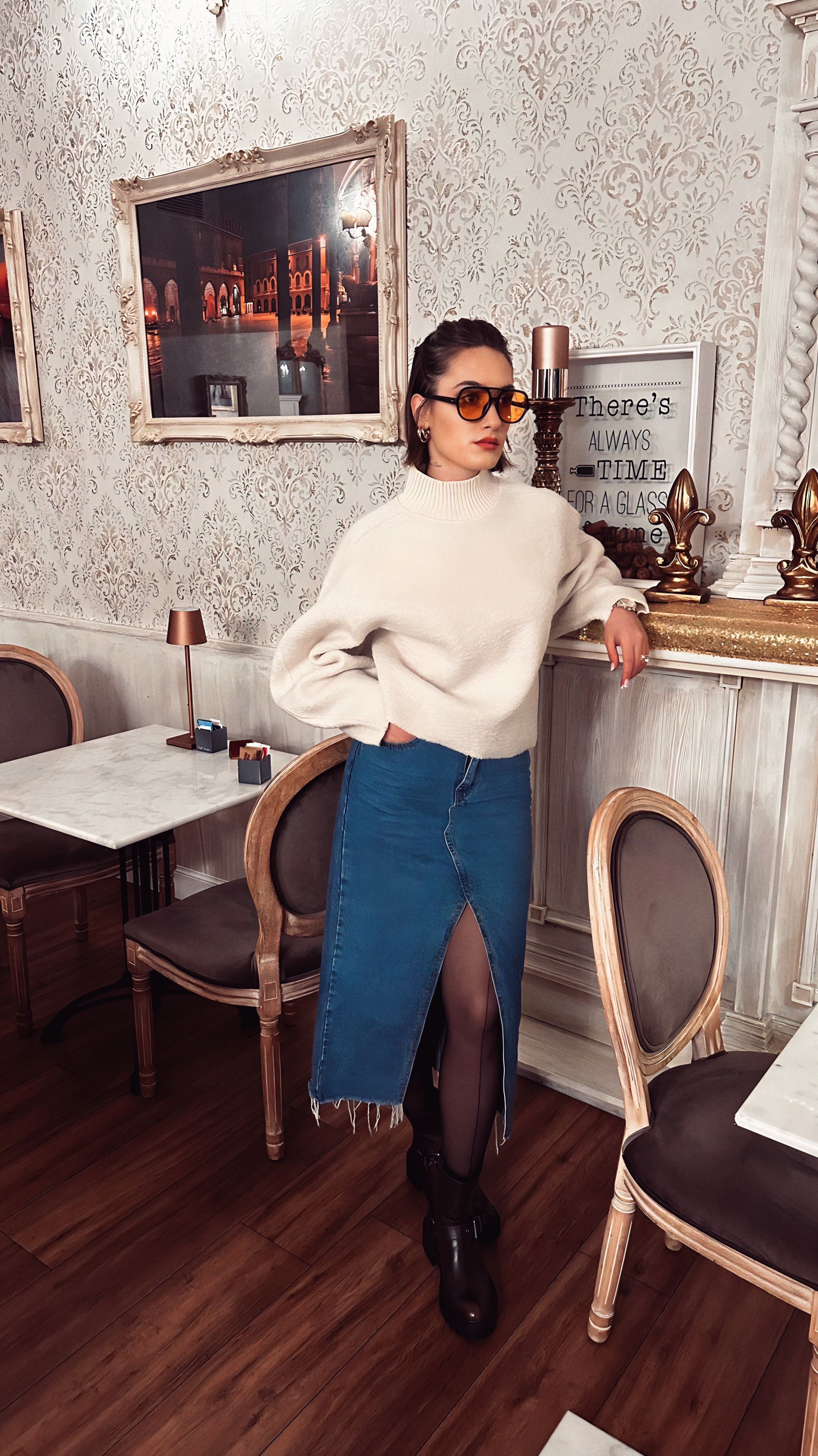 Mulher estilosa em um café rústico usando saia jeans e suéter.