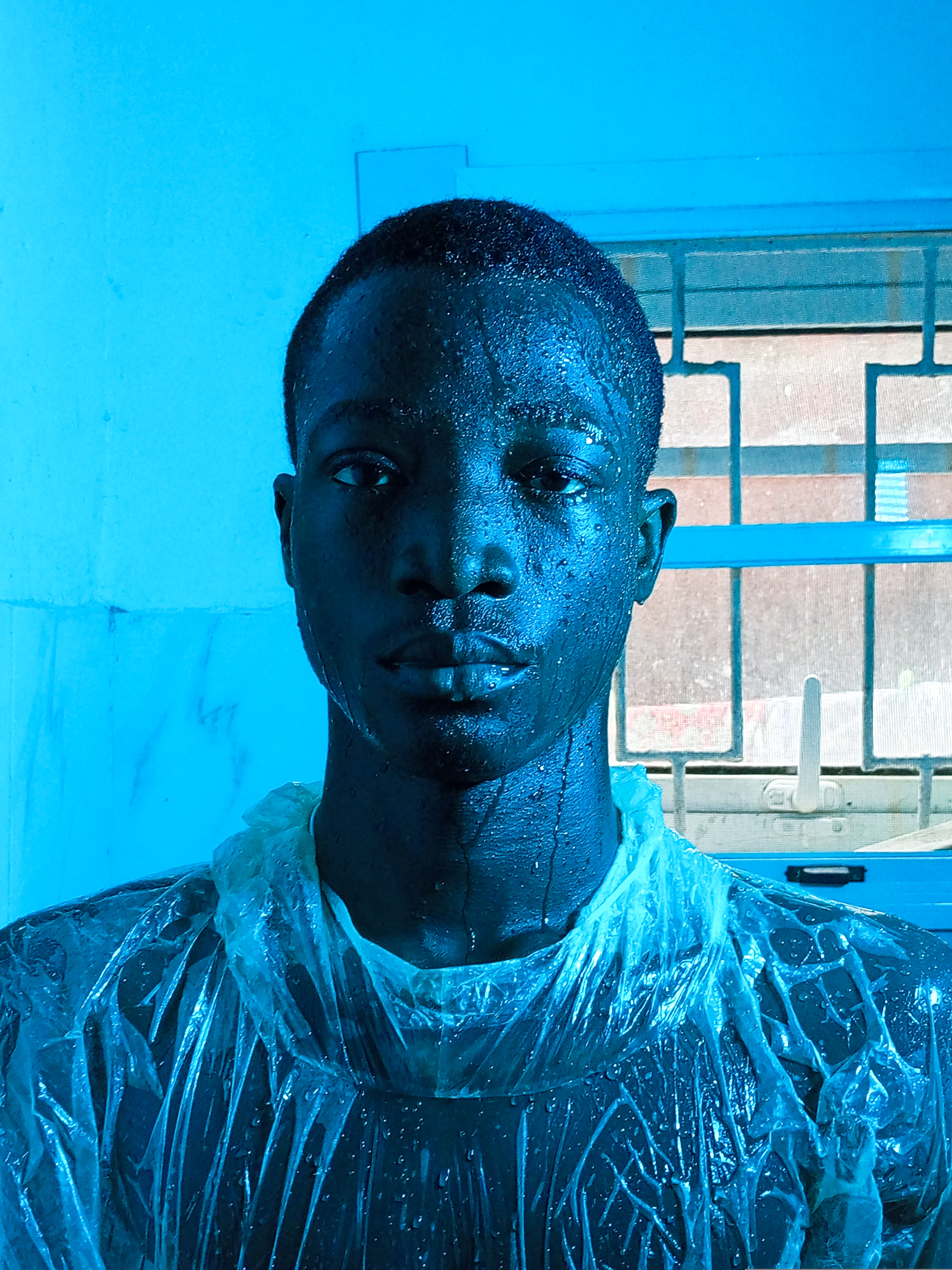 Artistic portrait of a man in blue lighting, wearing a plastic suit indoors.