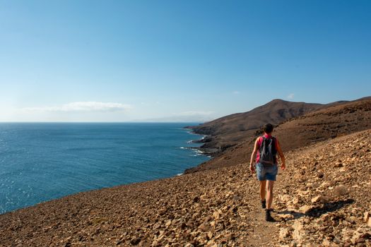 A lone hiker with a backpack walking the arid coastal path under a clear blue sky.