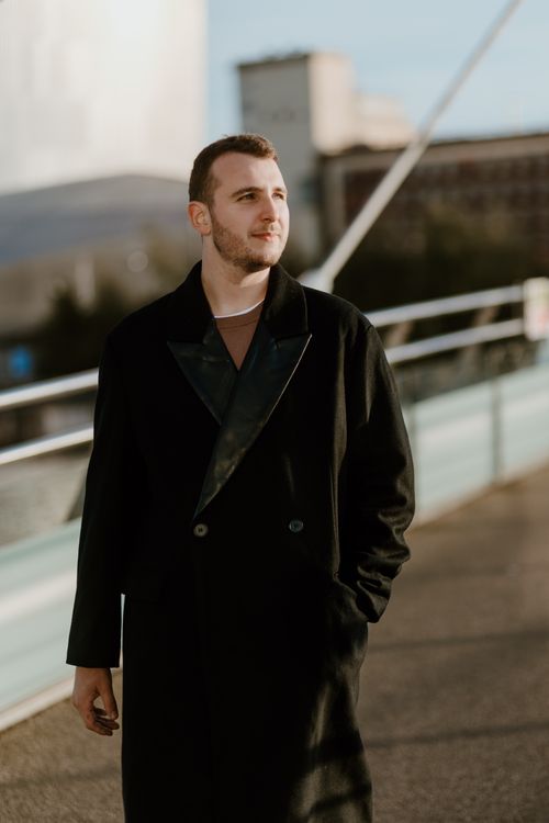 Free A young man in a black coat poses confidently on an urban bridge, exuding style and sophistication. Stock Photo