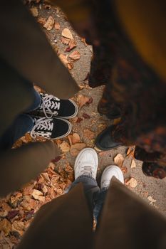 Top view of three people standing on fallen autumn leaves, showcasing trendy footwear.