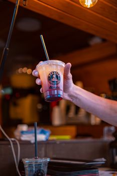 Person holding a colorful refreshing drink in a disposable cup at a cozy cafe setting.