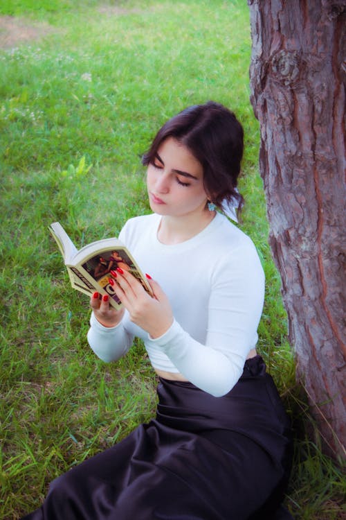 Young Woman Sitting on the Grass and Reading a Book 