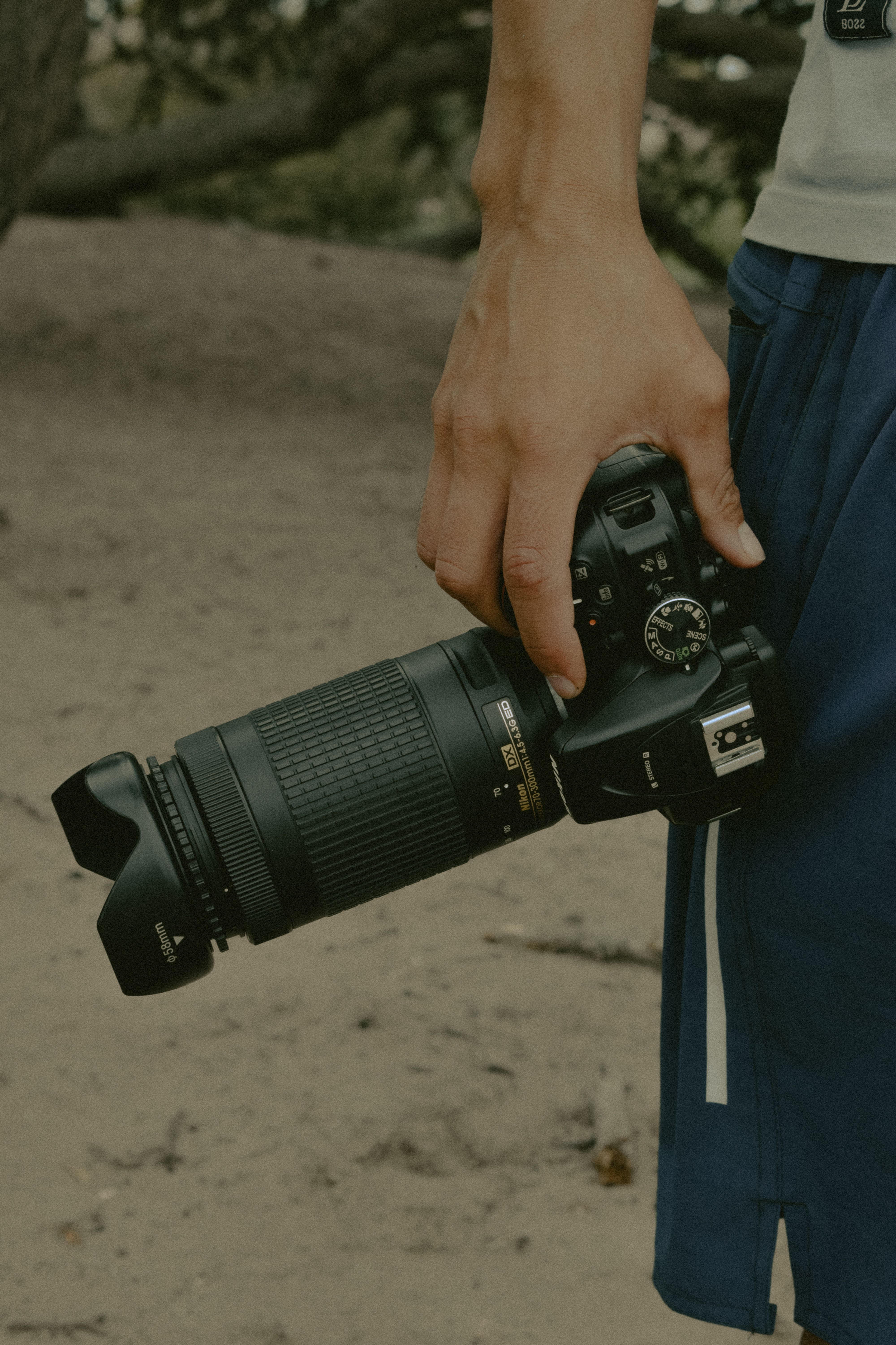 Man holding a DSLR camera with a long lens, captured outdoors in a natural setting.