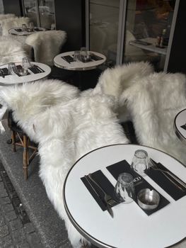 Elegant street cafe setup with white fur-covered chairs and tables, ready for dining.