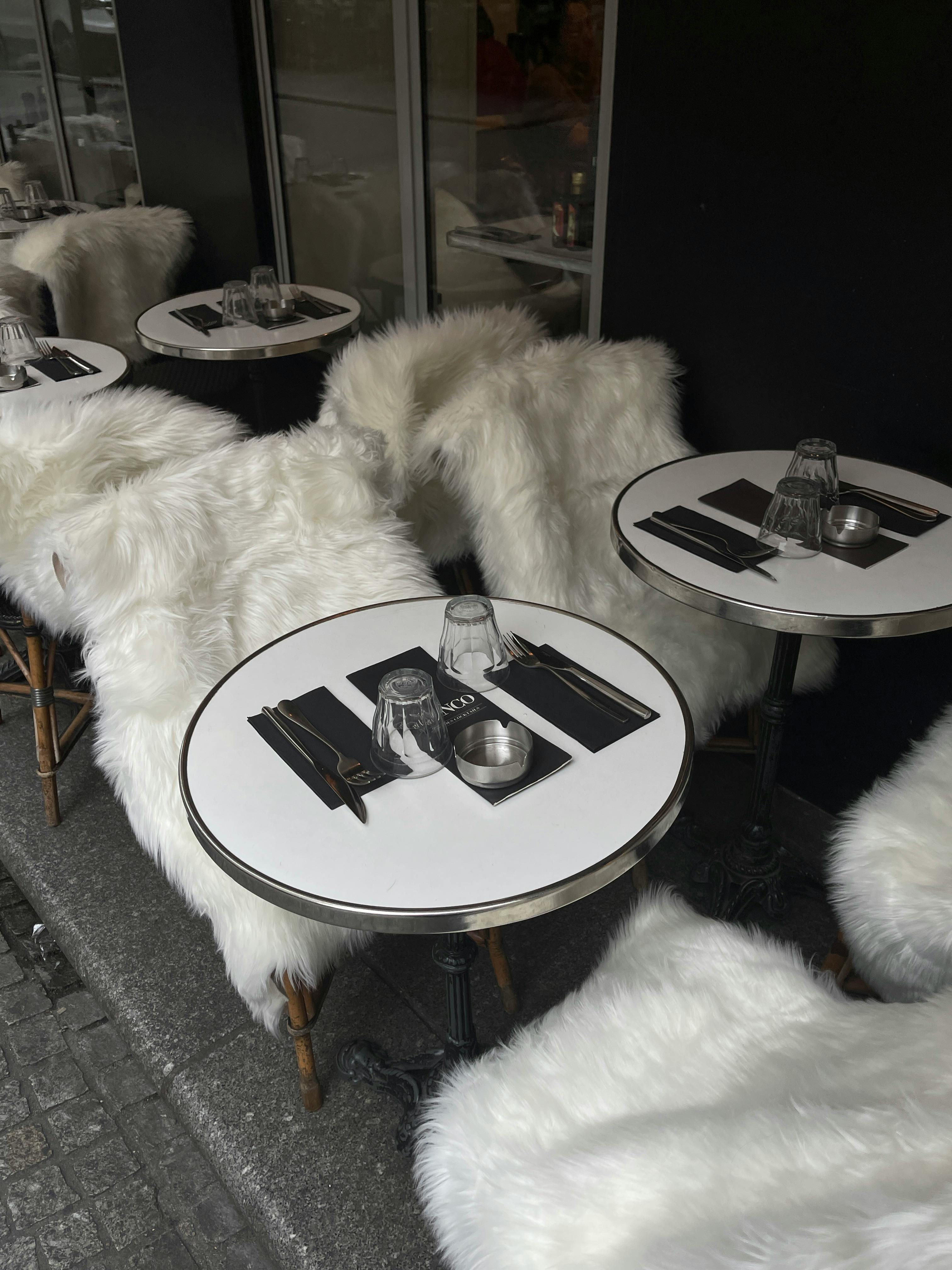 Modern café setting with fur-clad chairs and round tables on a city street.