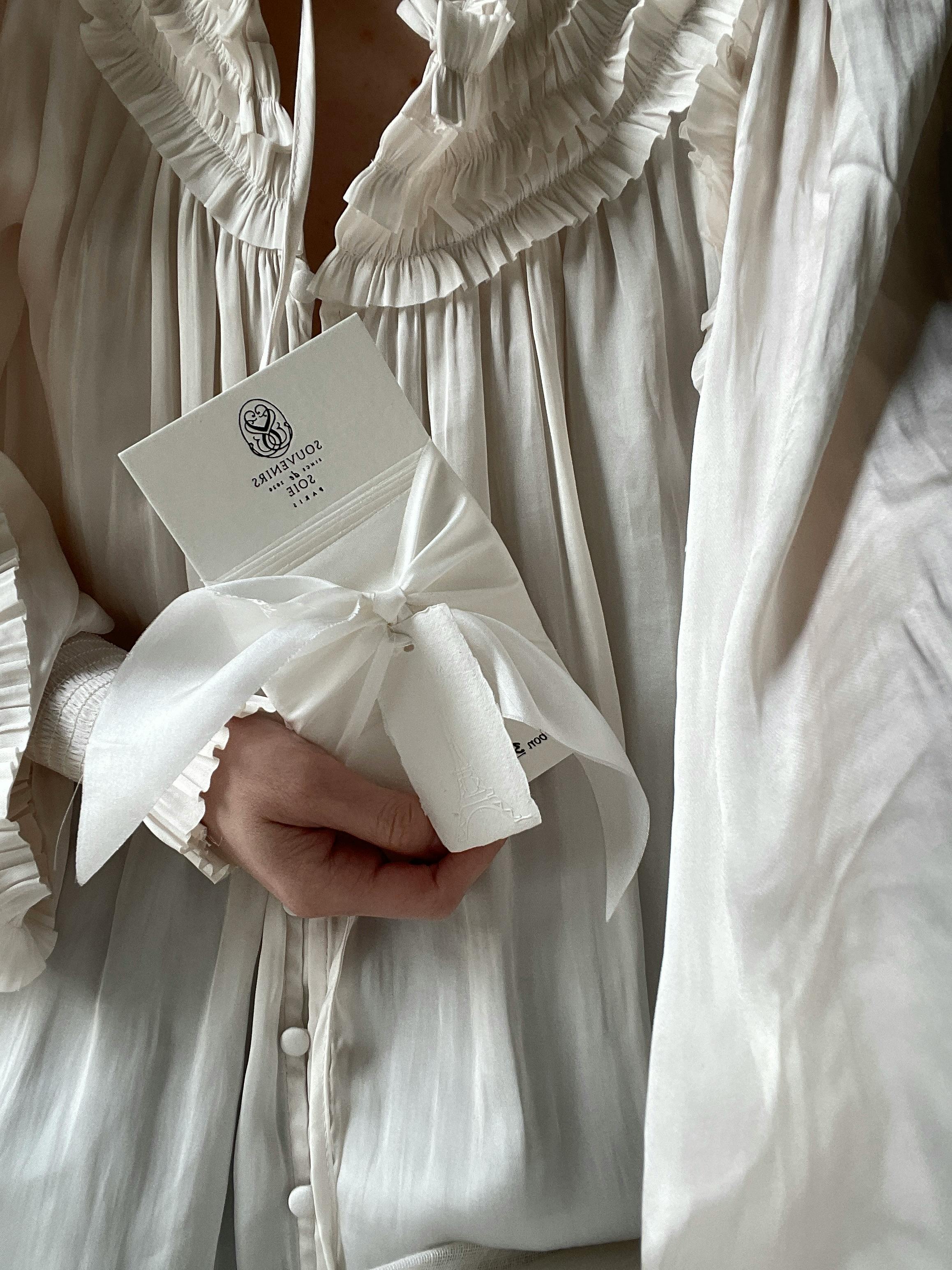 Close-up of a woman holding a white ribbon-tied gift card in luxurious nightwear.
