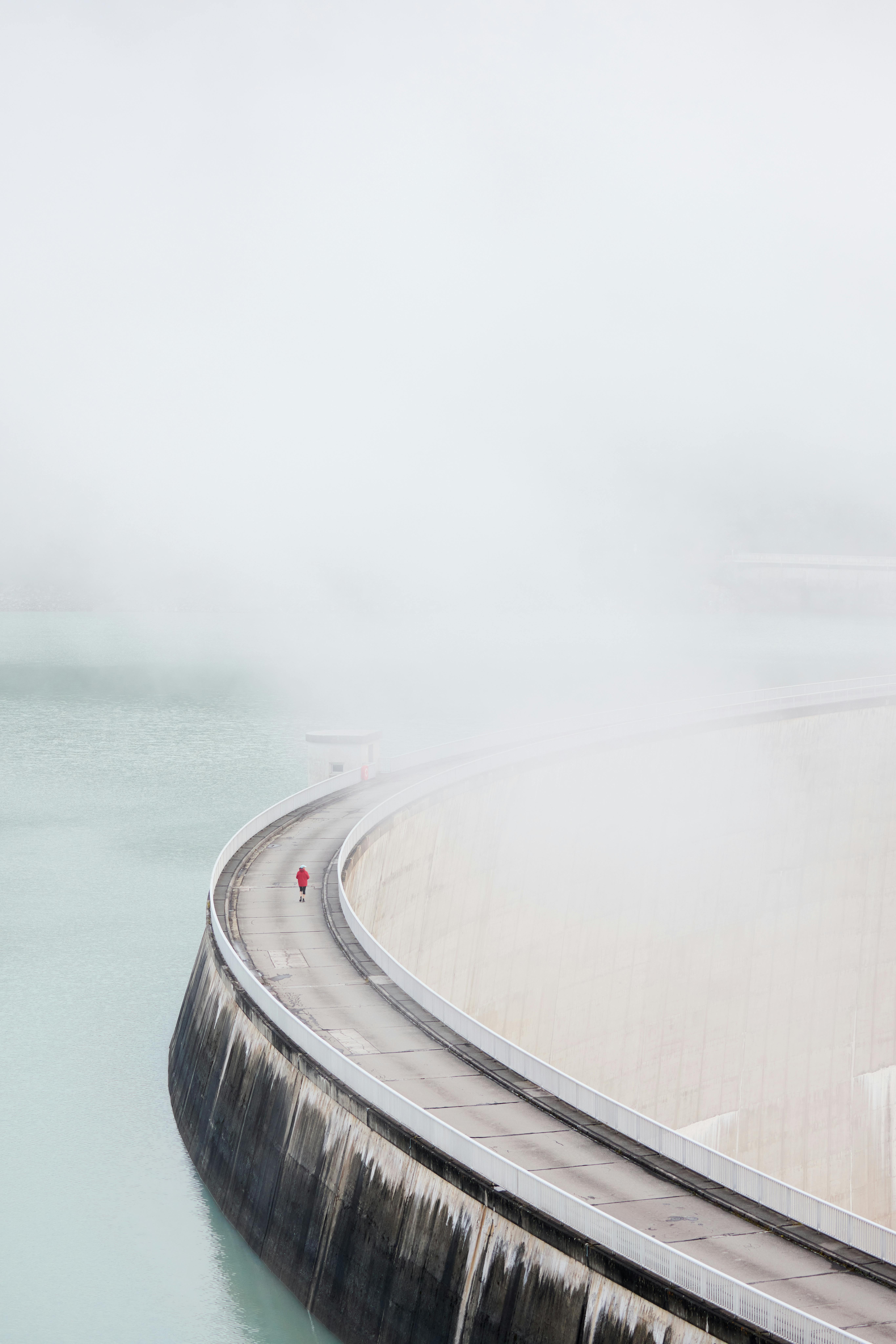 A lone jogger runs along the curve of the mist-covered Kaprun Dam in Austria, epitomizing tranquility.