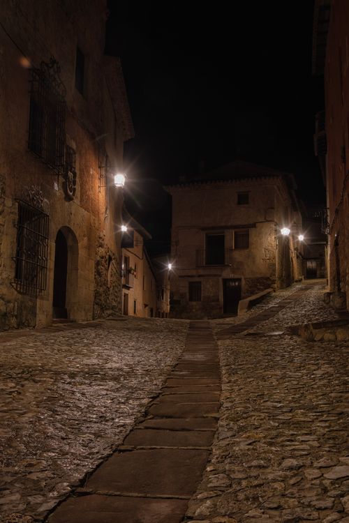 Free A tranquil, illuminated cobblestone alley in a Spanish town at night, showcasing traditional architecture. Stock Photo