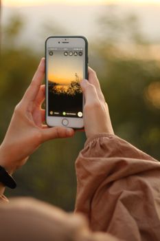 Hands holding a smartphone capturing a beautiful sunset in Sakarya, Türkiye.