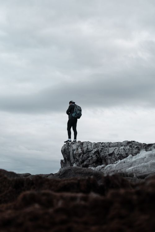 Free A lone hiker with a backpack stands atop a rugged cliff, embracing nature and the spirit of exploration. Stock Photo