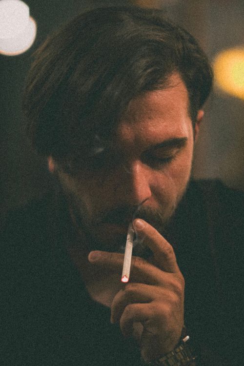 Free Dark and atmospheric portrait of a man smoking with a moody expression and dim lighting. Stock Photo