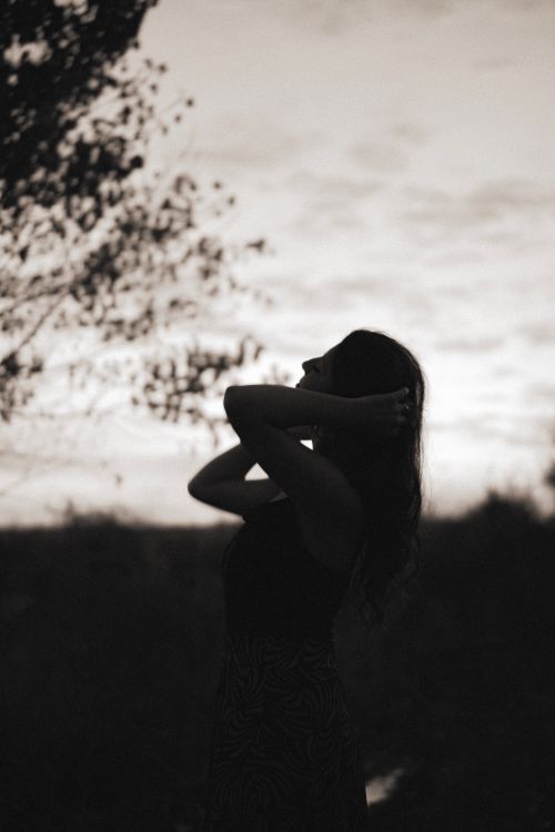 Free A dramatic black and white silhouette of a woman fixing her hair at dusk, adding to the mysterious ambiance. Stock Photo