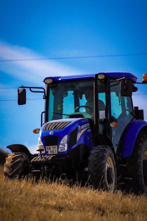 Free A vibrant blue tractor working in a sunny Turkish field with a bright blue sky backdrop. Stock Photo