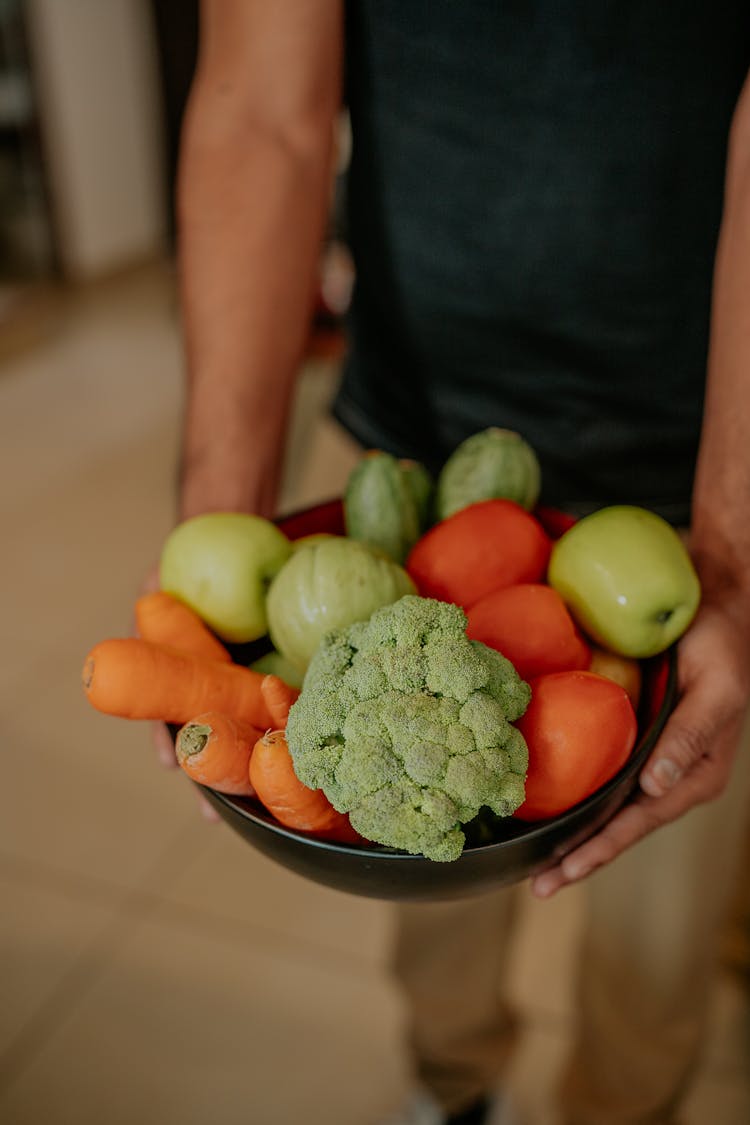 A Person Holding A Bowl With Fruit And Vegetables