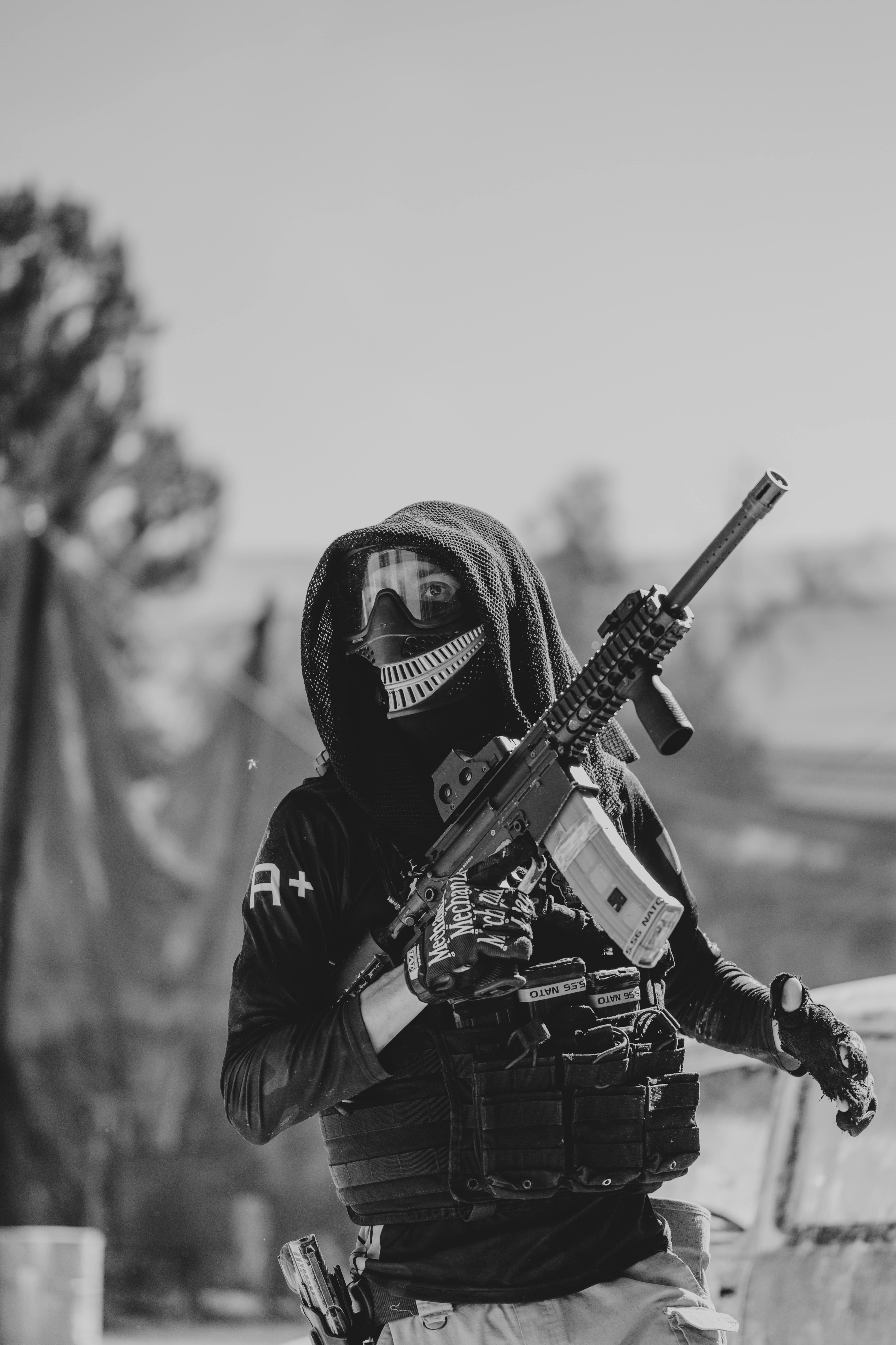 Photo dynamique en noir et blanc d'un joueur de paintball masqué tenant une réplique de pistolet pendant une partie. Prescription Goggle Inserts - Dynamic black and white photo of a masked paintball player holding a replica gun during a game.