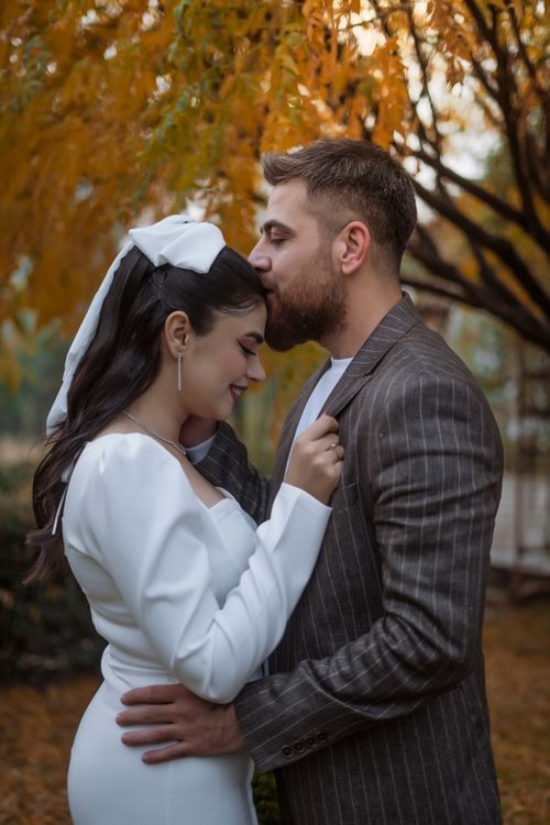 Free Bride and groom share a loving forehead kiss in a fall park setting. Stock Photo