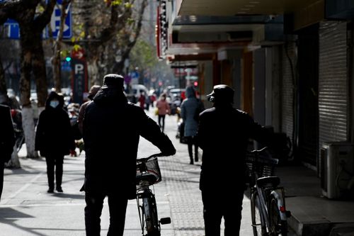 Free Silhouetted people walking bicycles along a city street, capturing urban life and movement. Stock Photo