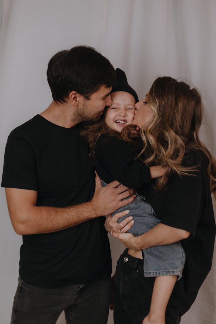 Mother And Father Kissing Smiling Daughter 