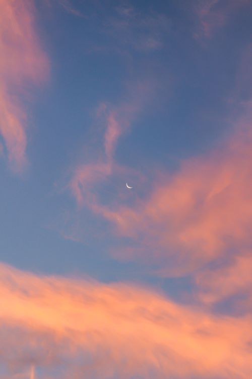 Free A vibrant sunset sky with puffy clouds and visible crescent moon. Stock Photo