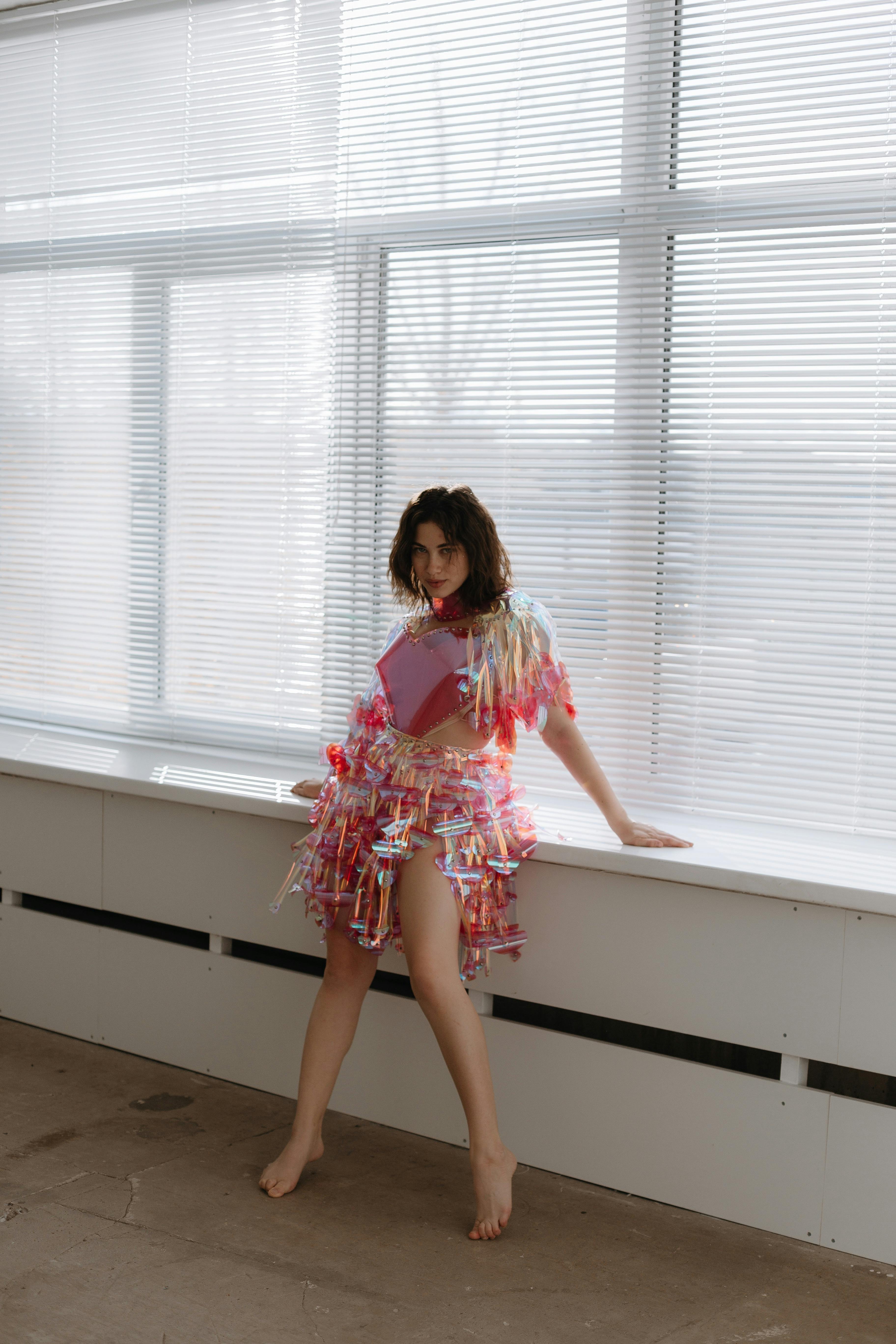 时尚模特穿着独特的彩色连衣裙，在室内大窗户前摆姿势