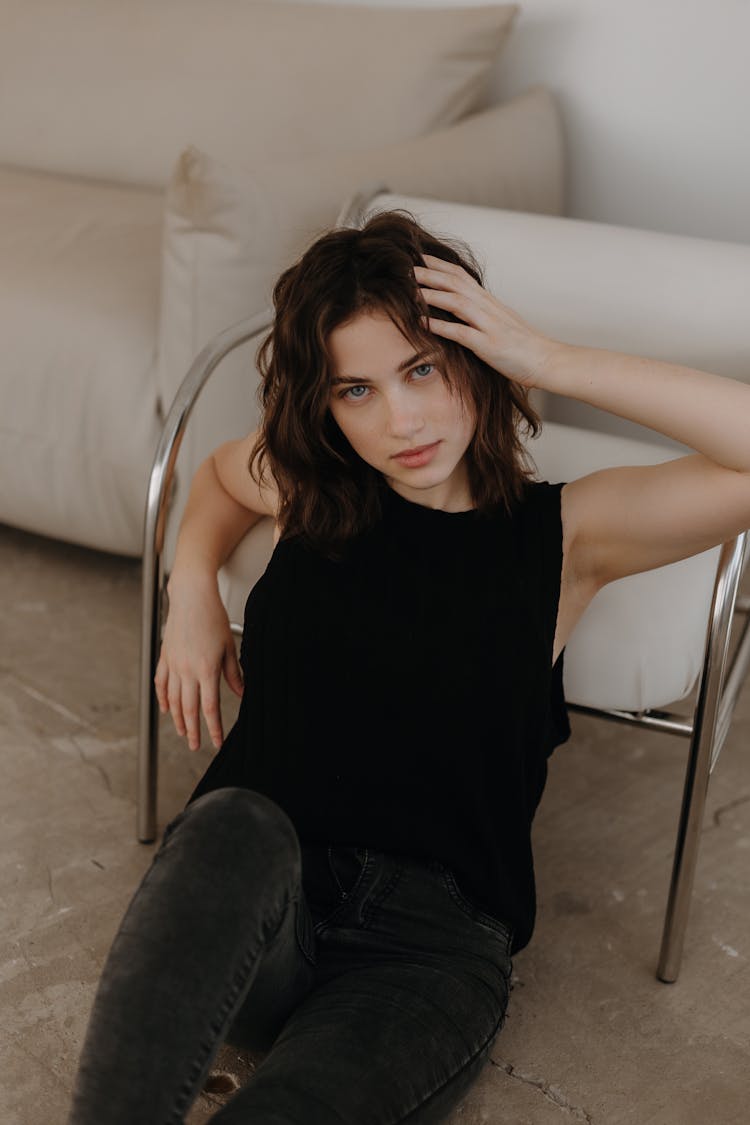 Brunette In Black Sitting On Stone Floor And Leaning On Chair