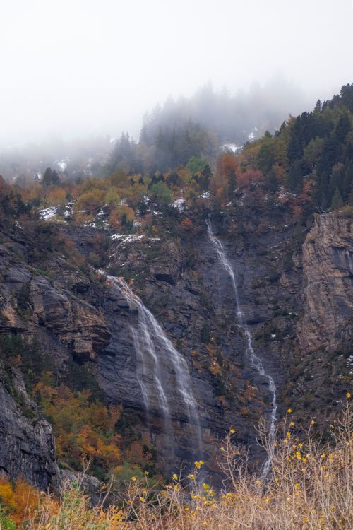 Free Capture of a stunning waterfall cascading down rocky cliffs amidst vibrant autumn foliage. Stock Photo