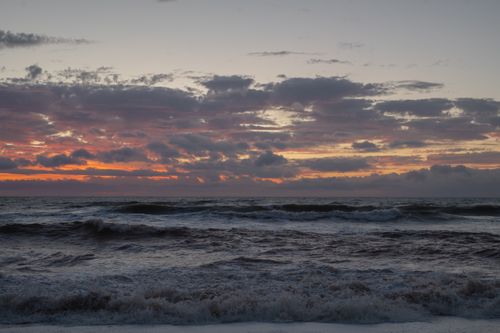 Free A stunning seascape at sunset featuring dramatic clouds and waves crashing against the shore. Stock Photo