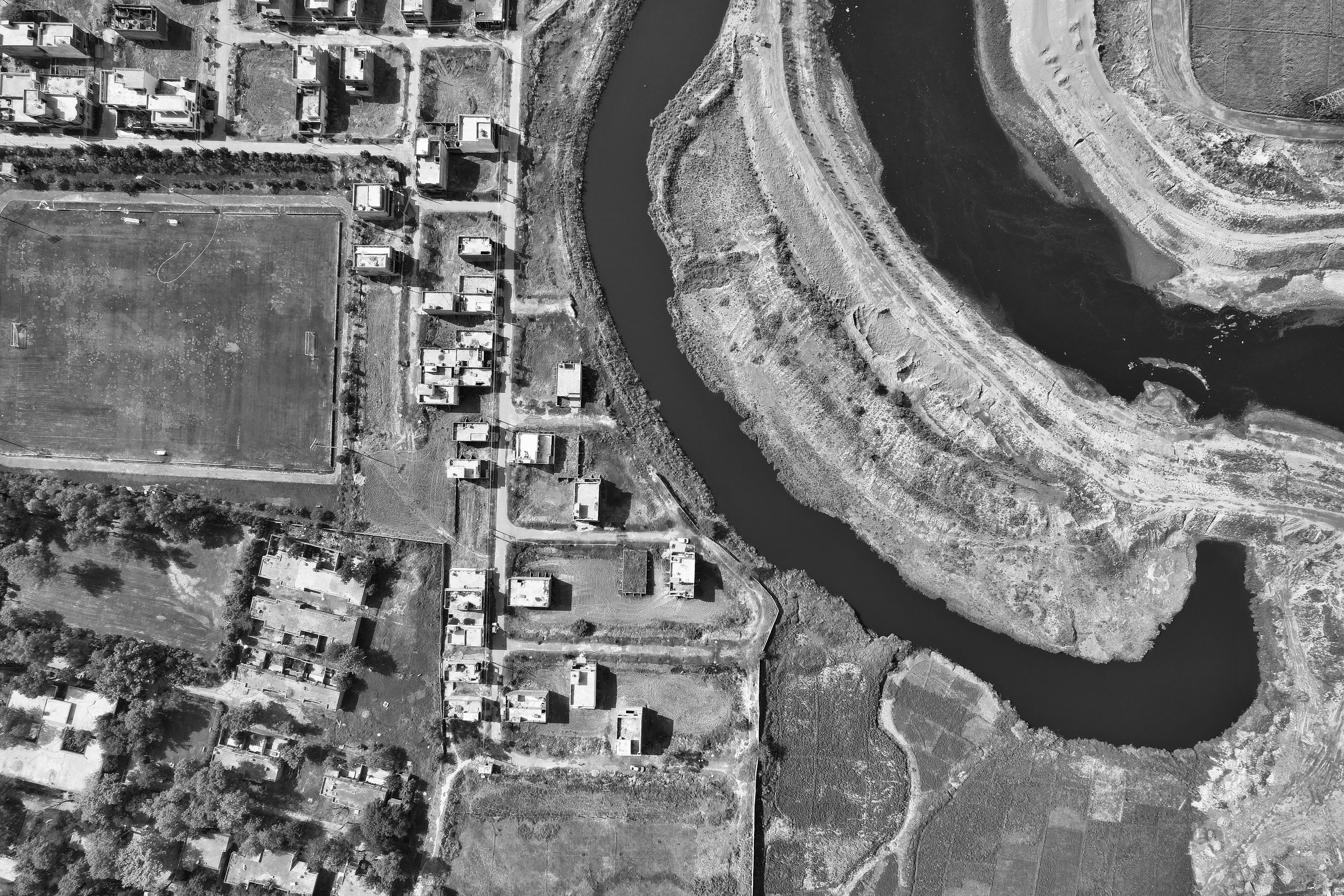 Black and white aerial shot of a river winding near houses in Kala Shah Kaku, Pakistan.