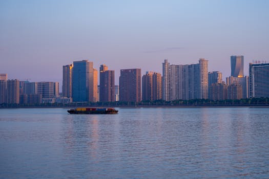 A scenic view of Hangzhou's skyline at dusk with a cargo ship on the river.