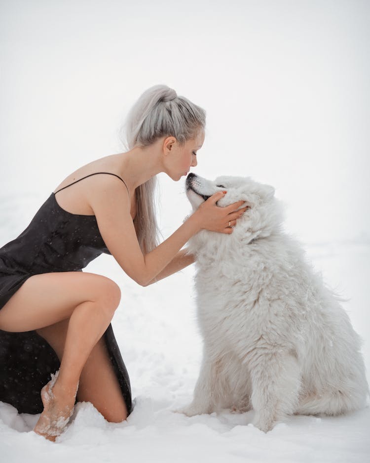 Beautiful Woman Kneeling In The Snow And Kissing A Dog 