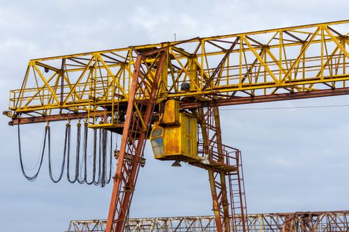 Free Close-up of a yellow industrial crane with openwork design against a cloudy blue sky. Stock Photo