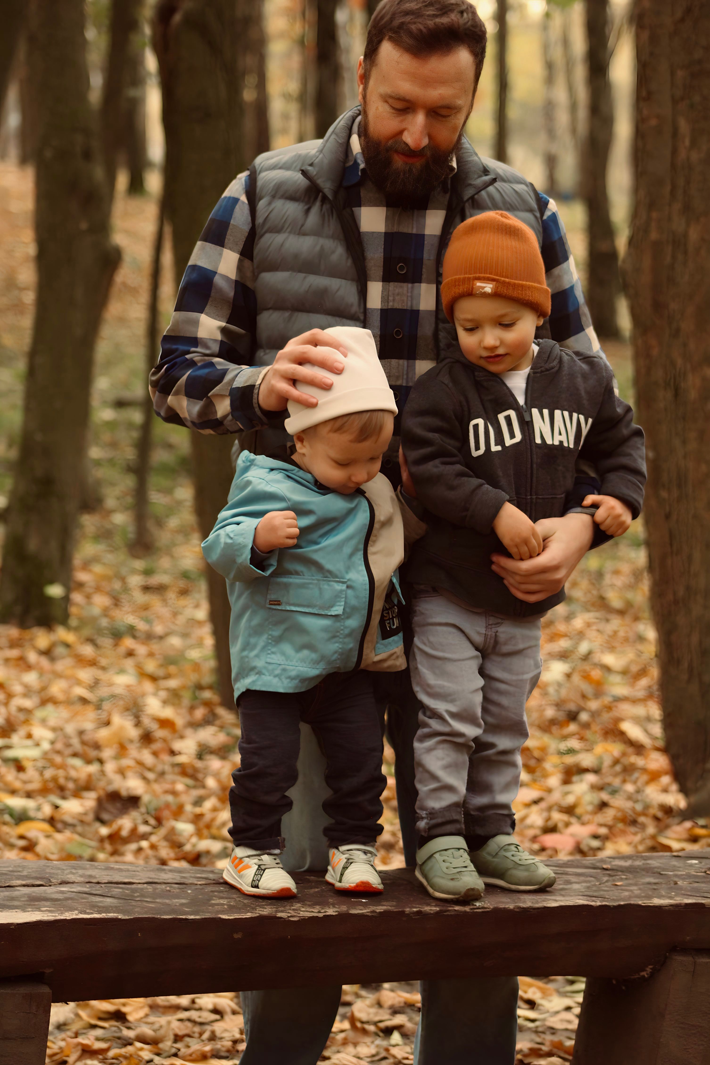 A father with two sons standing on a bench in a forest park during fall.