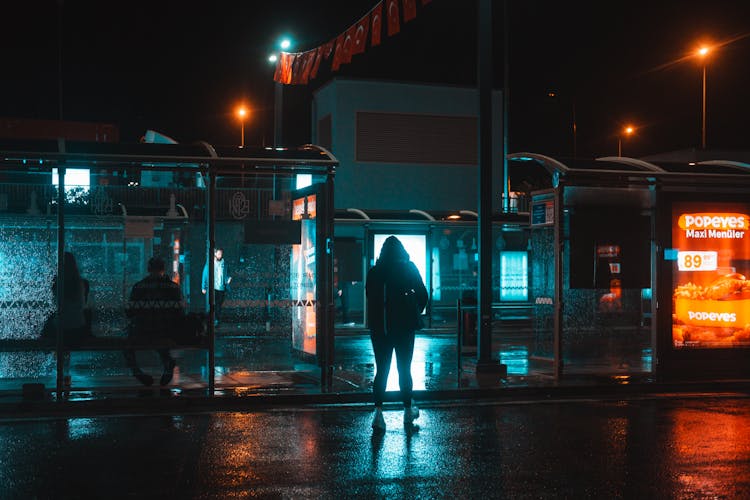 Silhouettes Of People Waiting At A Bus Stop On A Night City Street