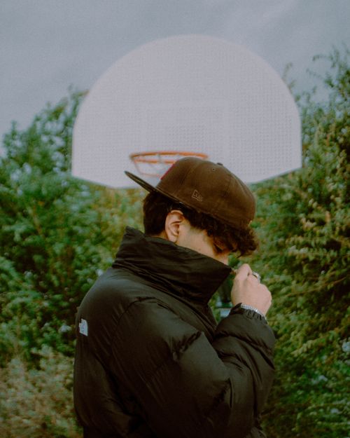 Free Young man in a puffer jacket standing near a basketball court hoop outdoors. Stock Photo