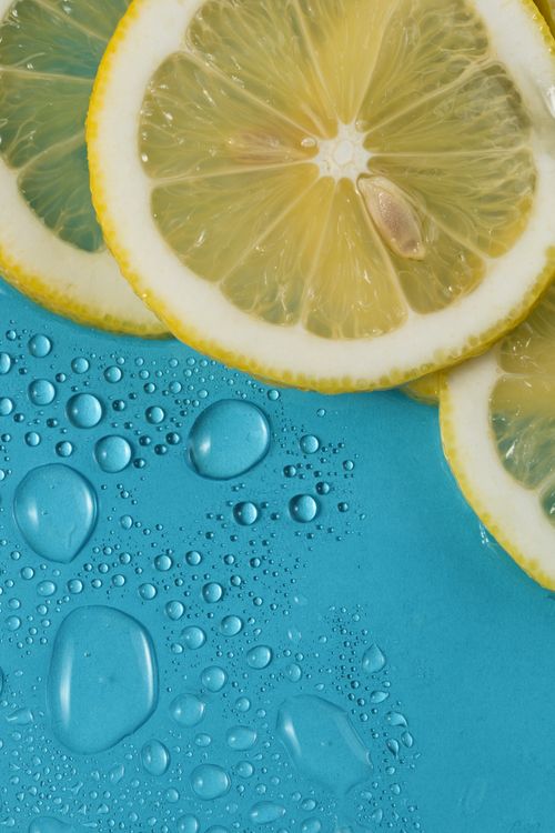 Free Close-up of vibrant lemon slices with refreshing water droplets on a blue background. Stock Photo