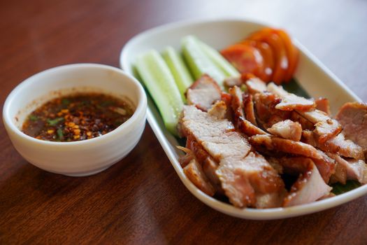 Close-up of grilled pork slices with cucumber, tomato, and dipping sauce for a flavorful meal.