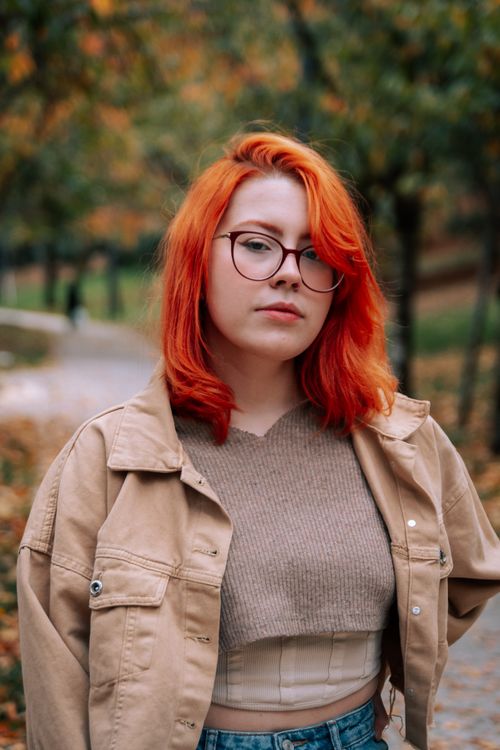 Free Stylish redhead woman wearing glasses and jacket in a scenic autumn park. Stock Photo